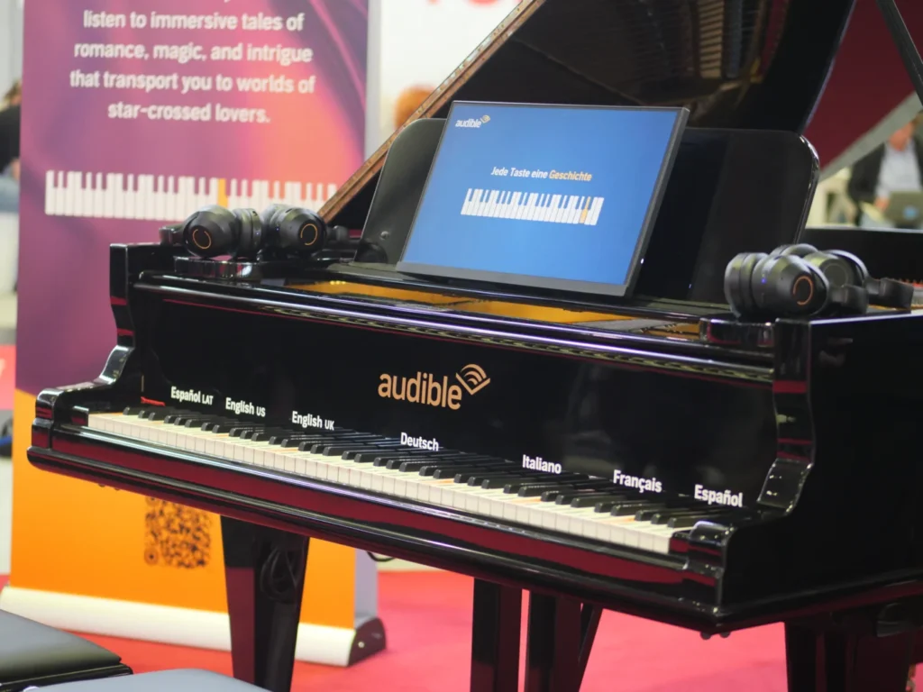 Ein schwarzes Klavier mit Kopfhörern und einem Bildschirm, der die Aufschrift 'Jede Taste eine Geschichte' trägt, bei der Buchmesse in Frankfurt.