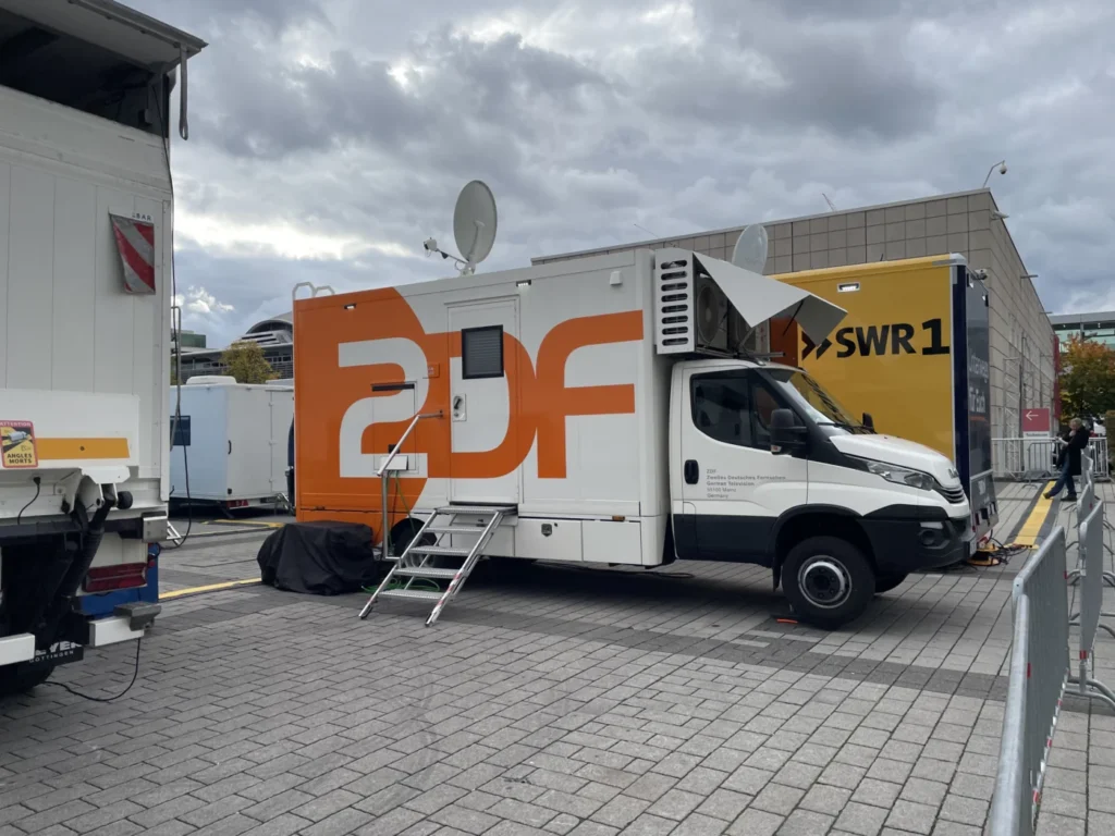 Ein Übertragungsfahrzeug des ZDF vor einem Messegebäude, umgeben von anderen Medienfahrzeugen.